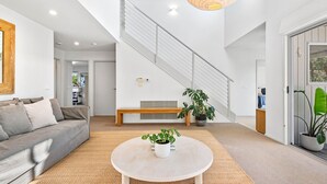 A modern living room with a sofa, a round coffee table with a plant, a staircase, and a large window. - Ocean Haven: 3  BR, 3  BA House in Sorrento, Sleeps 6 (Sorrento)