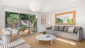 A modern living room with a sofa, a coffee table, and a large window offering a view of greenery. - Ocean Haven: 3  BR, 3  BA House in Sorrento, Sleeps 6 (Sorrento)
