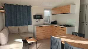 A compact living space with a kitchenette, a sofa, a dining table, and a TV. - Bungalow Neuf Superbe Terrasse Plein sud Face mer à l' ile d' or Camping 4 (Saint-Raphaël)