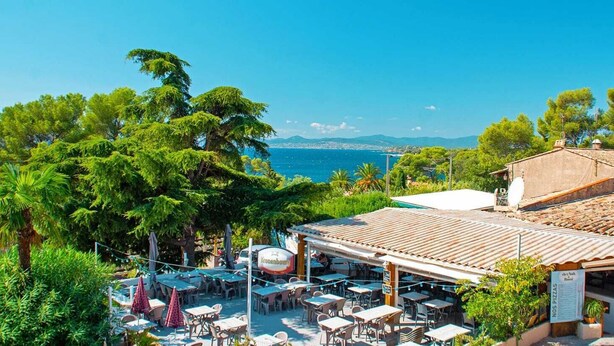 An outdoor cafe with tables and chairs, overlooking a coastal view with trees and a clear sky. - Bungalow Neuf Superbe Terrasse Plein sud Face mer à l' ile d' or Camping 4 (Saint-Raphaël)