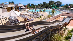 A water slide at a resort with a pool area, lounge chairs, and umbrellas. - Bungalow Neuf Superbe Terrasse Plein sud Face mer à l' ile d' or Camping 4 (Saint-Raphaël)