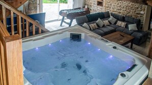 Un jacuzzi en una habitación con pared de piedra, escalera de madera y sofá con cojines.