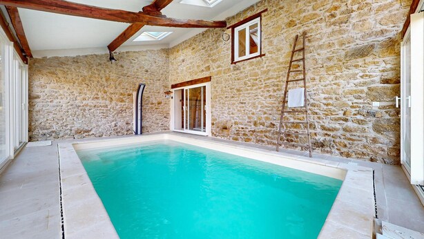 Una piscina interior con paredes de piedra y vigas de madera, un tragaluz y una escalera.
