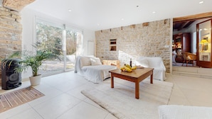 Un salón amplio con pared de piedra, muebles blancos y un ventanal grande.