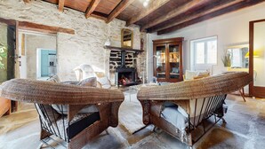 Una habitación rústica con pared de piedra, vigas de madera, chimenea, mobiliario de mimbre y un aparador de madera.