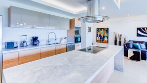 A modern kitchen with a large island, built-in appliances, and a dining area with a sofa and coffee table. - NEW Beach Club Game Room Cinema Condos (Nuevo Nayarit)