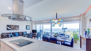 A modern kitchen with a large island, dining area with a view, and a living room with a sofa and artwork. - NEW Beach Club Game Room Cinema Condos (Nuevo Nayarit)