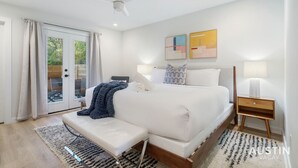 Une chambre à coucher moderne avec un grand lit, un banc, une table de chevet et un ventilateur de plafond.