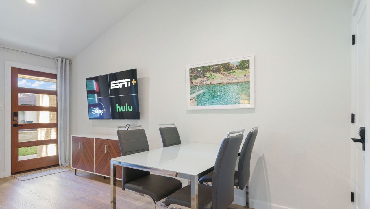 Un espace repas moderne avec une table blanche, des chaises noires et un téléviseur affichant les logos d’ESPN+ et de Hulu.