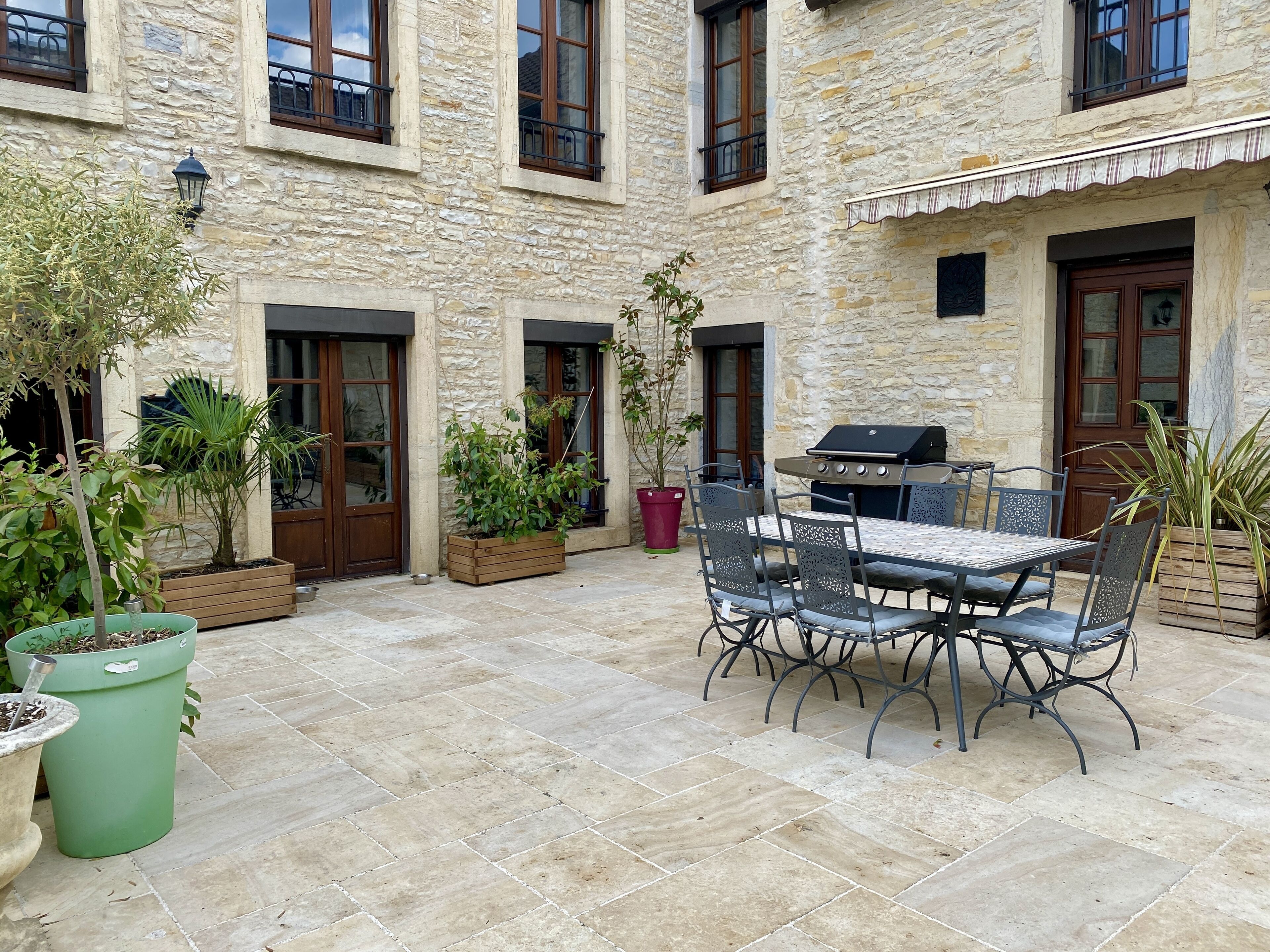 Ein Steinhaus mit einer Terrasse, die einen Tisch, Stühle, Kübelpflanzen und einen Grill umfasst.