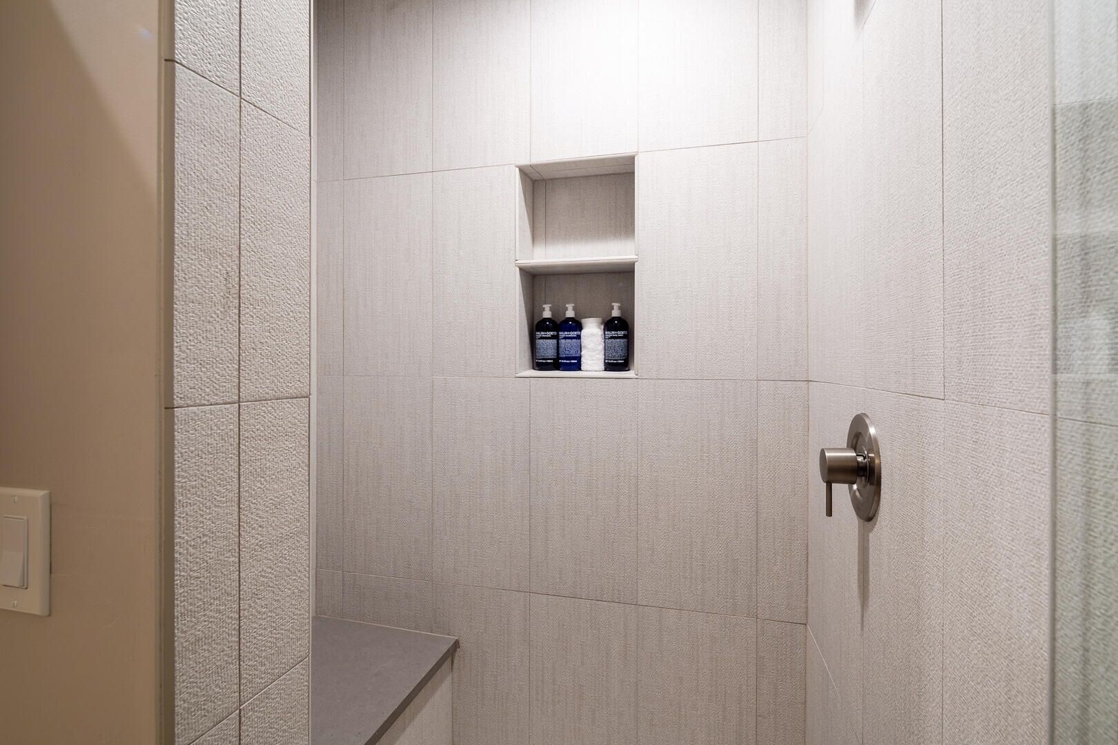 A modern bathroom with a shower area, a built-in shelf with toiletries, and a door with a handle.