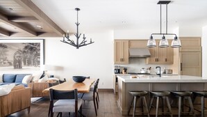 Eine moderne Küche mit Holzausstattung, einer zentralen Kochinsel mit Barhocker und einem Essbereich mit Holztisch und -stühlen.