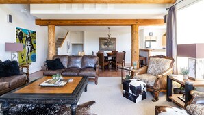 A spacious living room with a high ceiling, exposed wooden beams, a leather sofa, a patterned armchair, and a coffee table. - Saddle Ridge V2 3 Bedroom Condo by Moonlight Basin Lodging (Big Sky)
