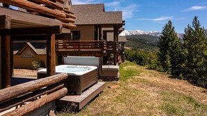 A log cabin with a hot tub and a deck overlooking a mountainous landscape. - Saddle Ridge V2 3 Bedroom Condo by Moonlight Basin Lodging (Big Sky)
