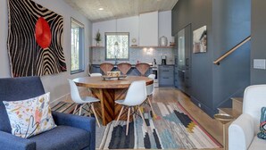 A modern kitchen with a wooden dining table, white chairs, and a colorful rug.