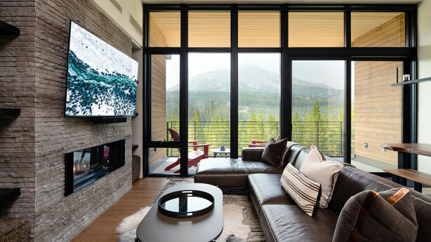 Ein modernes Wohnzimmer mit Kamin, großen Fenstern und Bergblick.