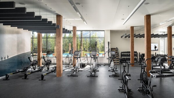 Un gimnasio con equipo de ejercicio variado, ventanas amplias y una escalera.