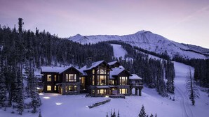 Een groot, meerhoog hotel met een stenen gevel en veel ramen, omringd door met sneeuw bedekte bomen en een berg op de achtergrond.