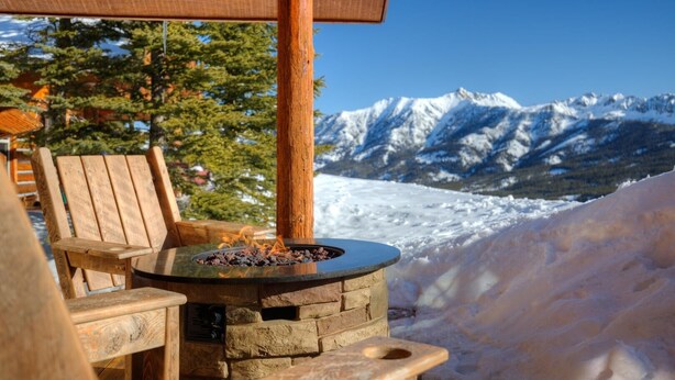 A wooden chair and a stone fire pit with a view of snow-covered mountains.