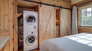 A wooden cabin room with a bed, a washing machine, and a sliding door closet.