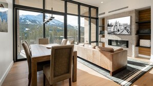 Una sala de estar moderna con un ventanal grande, una chimenea y un televisor montado en la pared.