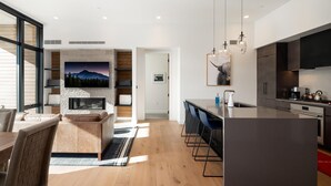 Una cocina moderna con una isla central, un comedor con sofá y sillones, y una sala de estar con chimenea y televisor.