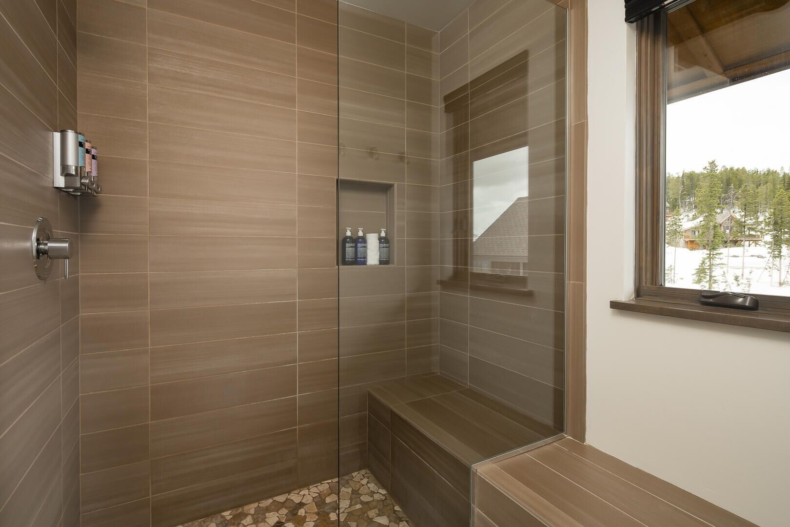 A modern bathroom with a shower area, a bench, and a window with a view of trees and buildings.