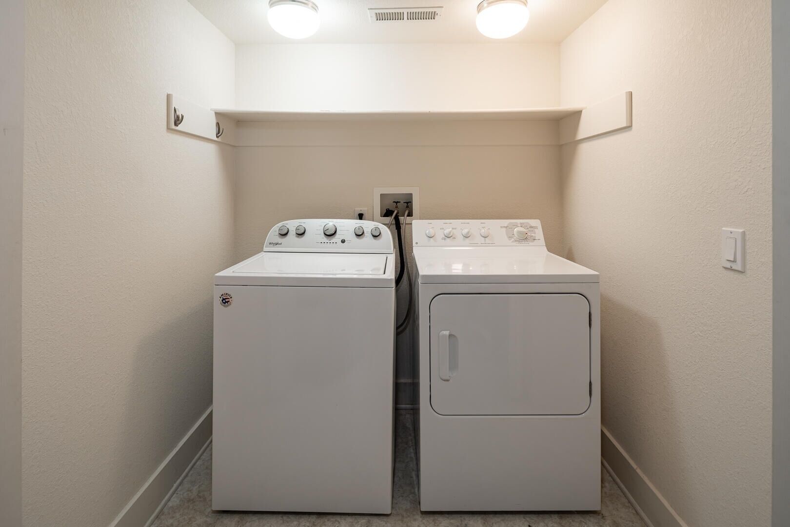 Una lavandería con dos lavadoras y secadoras Whirlpool blancas, una pared blanca y un respiradero en el techo.