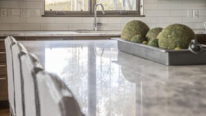 A kitchen with a marble countertop, a sink, and a window with a view of trees. - 18 Alpine Bend 6 Bedroom Home by Moonlight Basin Lodging (Big Sky)
