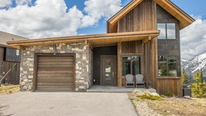 A modern two-story house with a stone facade, a large garage, and a front porch with chairs. - 18 Alpine Bend 6 Bedroom Home by Moonlight Basin Lodging (Big Sky)