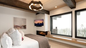 Une chambre moderne avec un grand lit, une cheminée et une grande fenêtre donnant sur la forêt.
