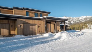Un bâtiment moderne aux murs extérieurs en bois et aux grandes portes de garage, se dressant sur fond de montagnes enneigées.