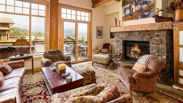 A spacious living room with a fireplace, large windows, and a balcony with outdoor seating.