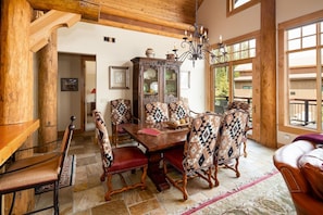 Cozy dining area with a wooden table and six chairs, surrounded by exposed beams and large windows.