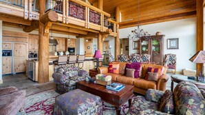 A spacious living area with a high ceiling, wooden beams, a dining area, and a kitchen with wooden cabinets.