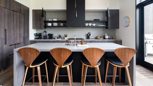 A modern kitchen with dark wood cabinets, a central island with bar stools, and a large window providing natural light.