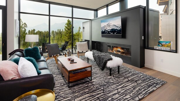 A modern living room with a fireplace, large windows, and a mountain view.