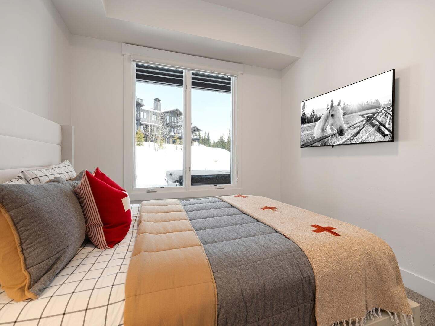 Une chambre à coucher avec un lit, des oreillers, une fenêtre donnant sur des immeubles et un tableau encadré accroché au mur.