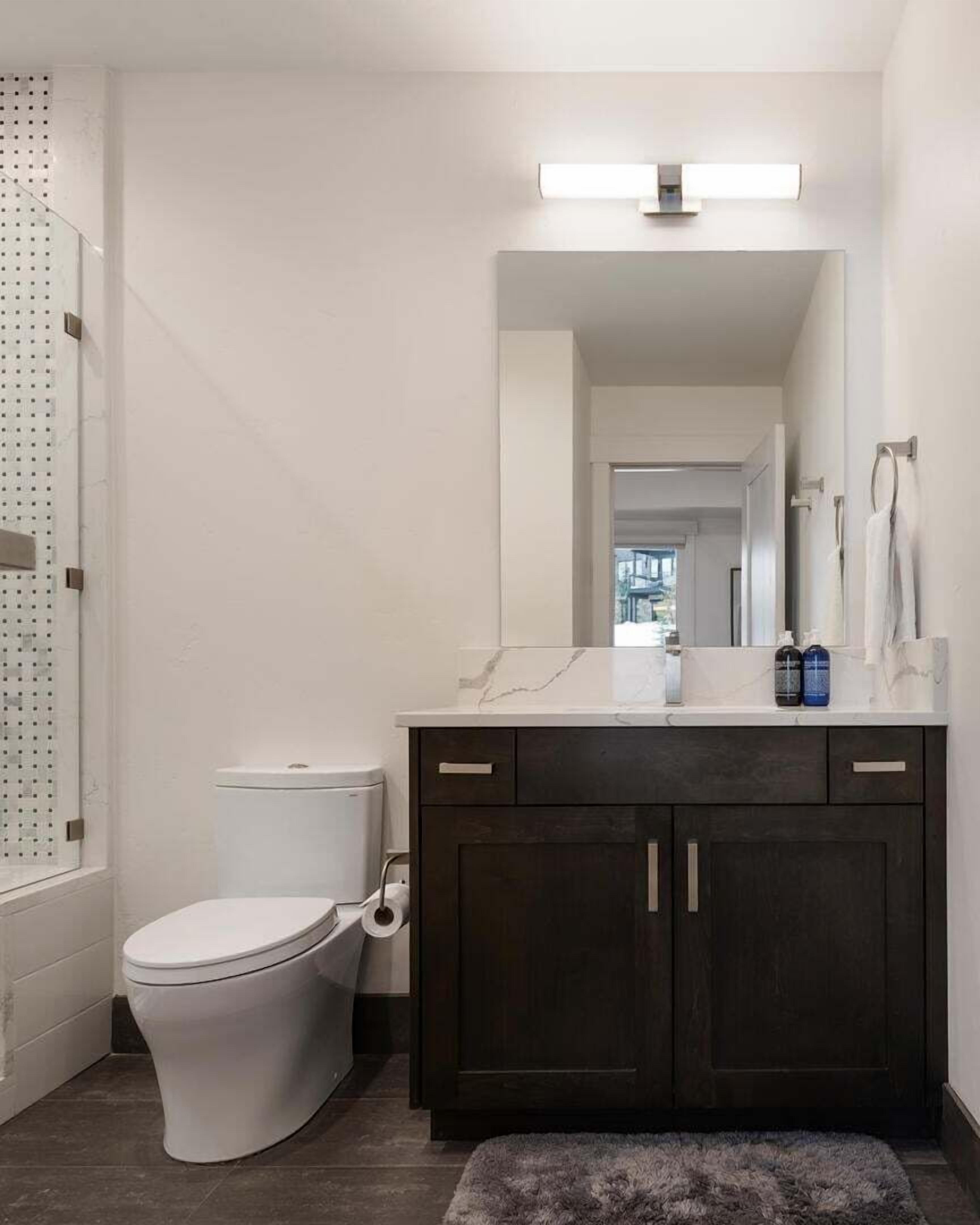Un baño moderno con inodoro, tocador de madera oscura y zona de ducha.