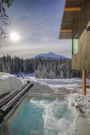 A hot tub with a view of a snowy mountain and forest.