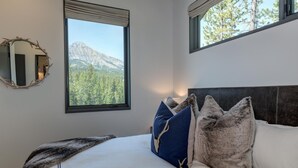 A bedroom with a bed, a large window with a mountain view, a mirror, and a headboard. - 17 Lake Cabin 3 Bedroom Home by Moonlight Basin Lodging (Big Sky)