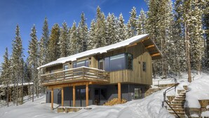 A modern wooden cabin with a balcony, surrounded by snow-covered trees. - 17 Lake Cabin 3 Bedroom Home by Moonlight Basin Lodging (Big Sky)