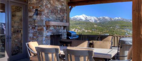 An outdoor patio with stone walls, a stone fireplace, and a view of snow-capped mountains.