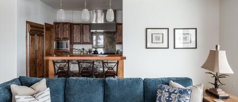 Un soggiorno moderno con un divano blu, travi in legno al soffitto, una cucina con mobili in legno e un'area pranzo.