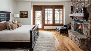 A bedroom with a large bed, a fireplace, and a window with a view of the outdoors.