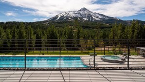 A pool area with a view of a snow-capped mountain, surrounded by trees and a fence. - 212 Lakelodge 3 Bedroom Condo by Moonlight Basin Lodging (Big Sky)