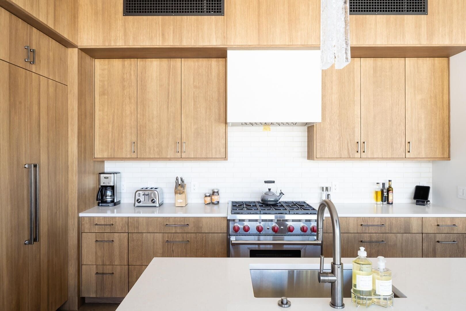 A modern kitchen with wooden cabinets, a stainless steel sink, a gas stove, and a coffee maker.