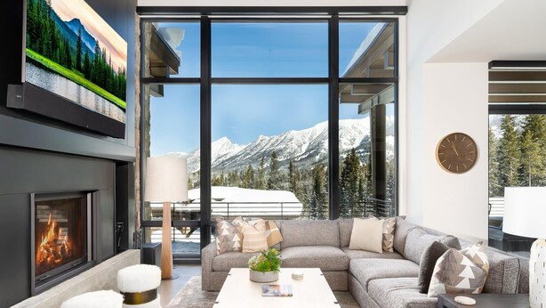 Un salon moderne doté d’une cheminée, de grandes fenêtres offrant une vue sur les montagnes, d’un canapé et d’une table basse.
