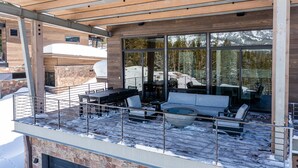 Une terrasse extérieure moderne, agrémentée d’une pergola en bois, d’un espace salon avec un canapé et des fauteuils, et d’une grande baie vitrée offrant une vue sur un paysage enneigé.