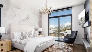Une chambre moderne avec un grand lit, une vue sur les montagnes, une cheminée et un mur en pierre.